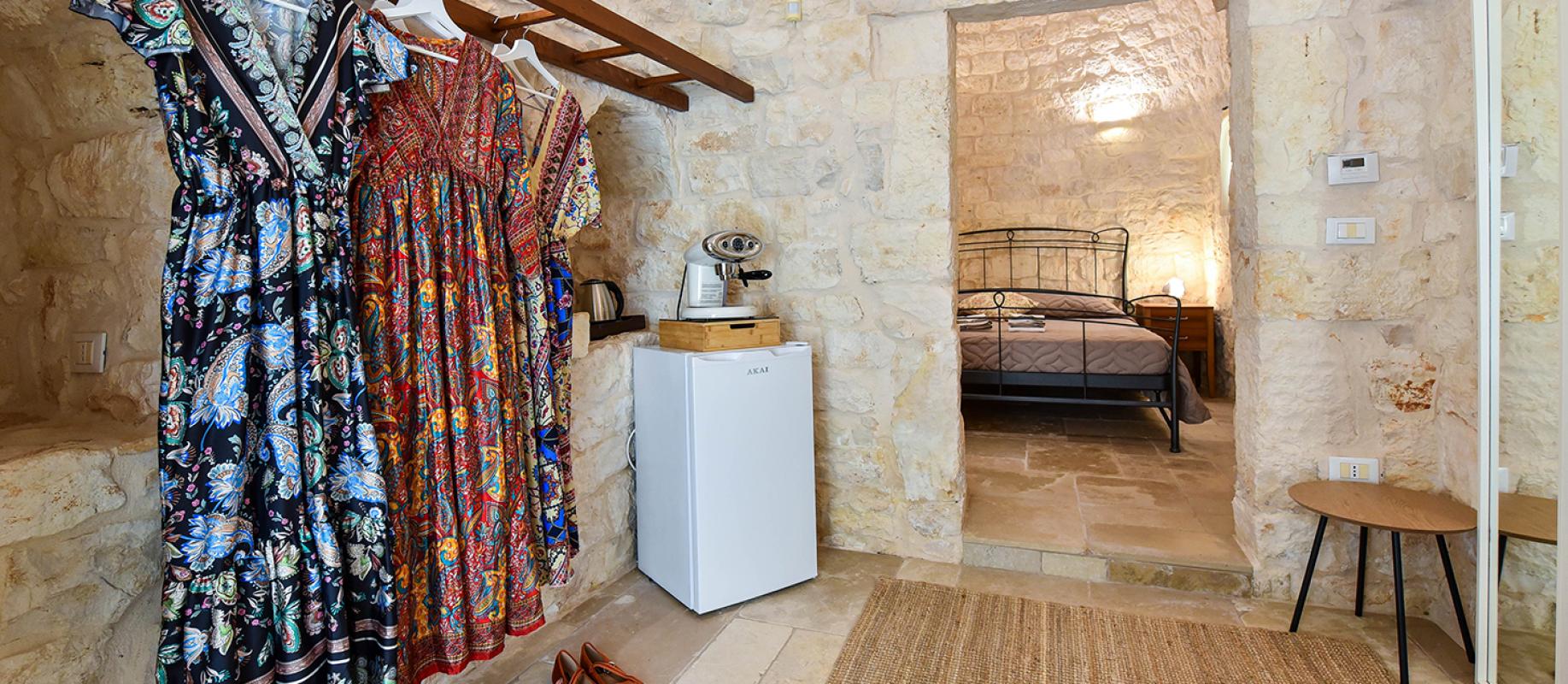 Rustikales Zimmer mit bunten Kleidern, gemütlichem Bett und warmer Atmosphäre.