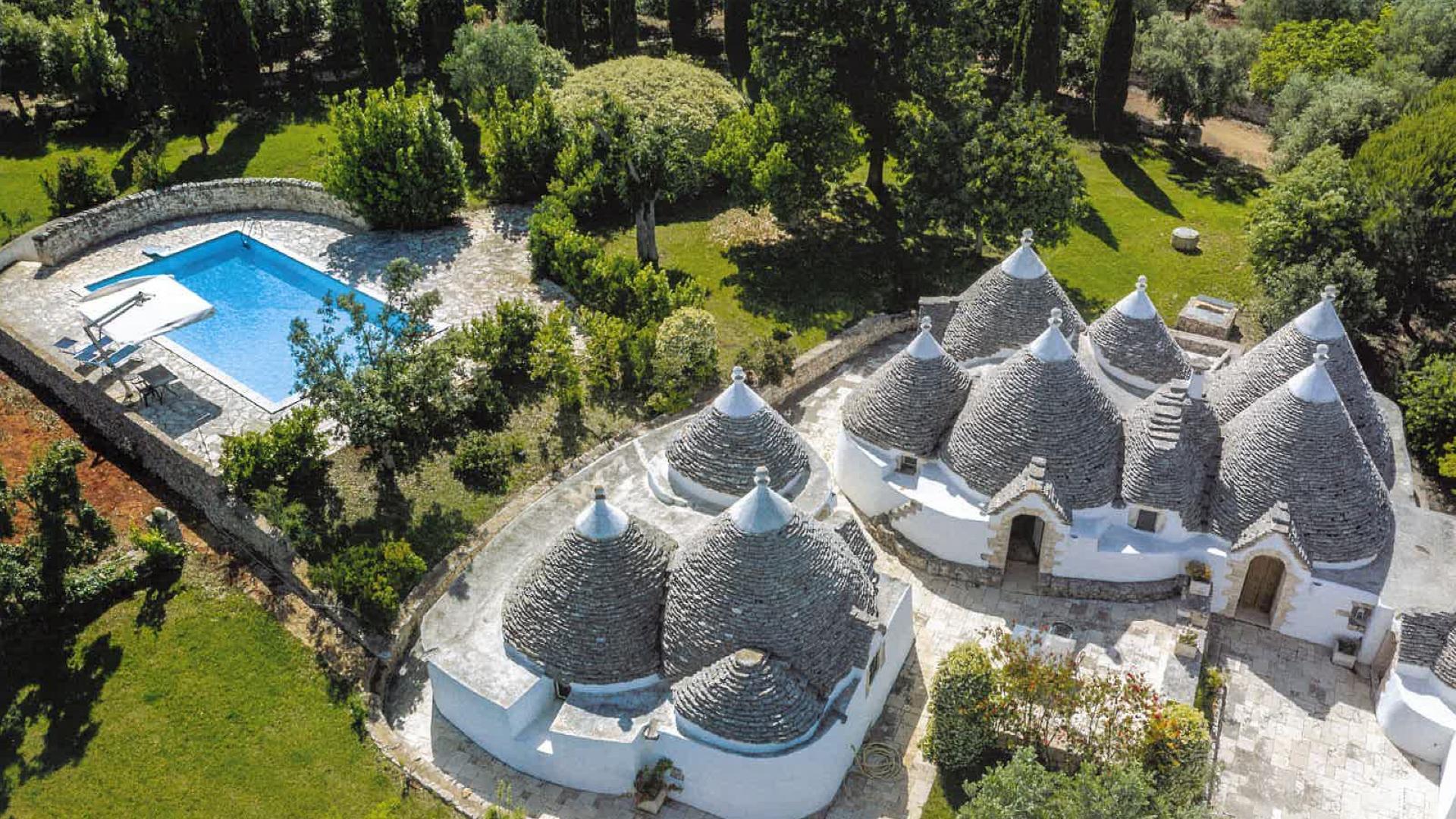 Trulli con piscina circondati da un giardino verde, tipici della Puglia.