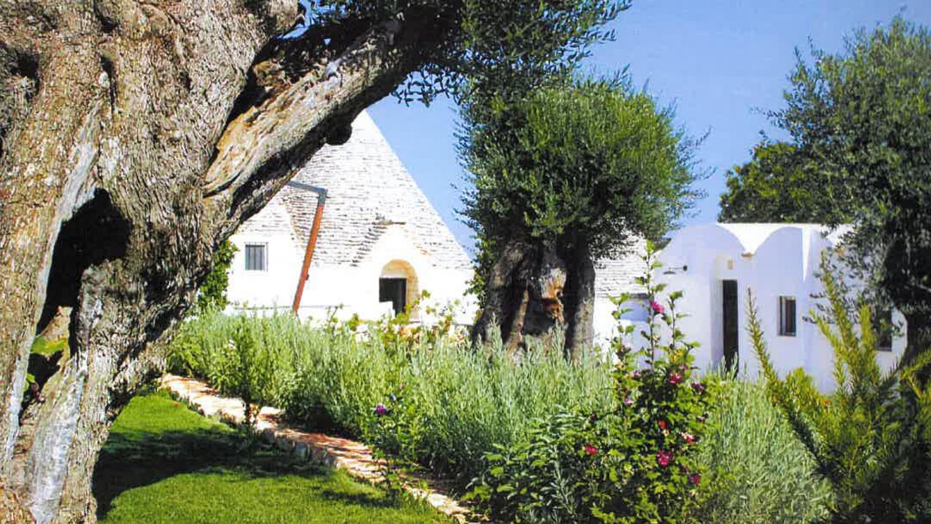 Trullo con giardino verde e alberi, tipica architettura pugliese.