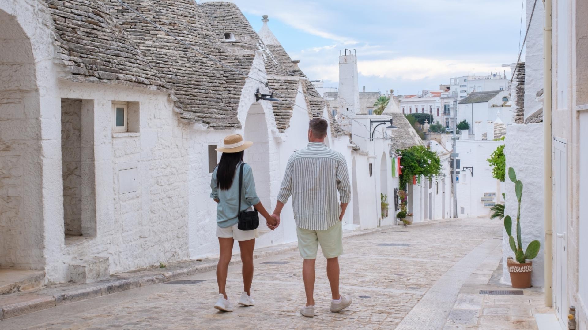 Coppia passeggia tra i trulli di Alberobello, Puglia, in un'atmosfera pittoresca.