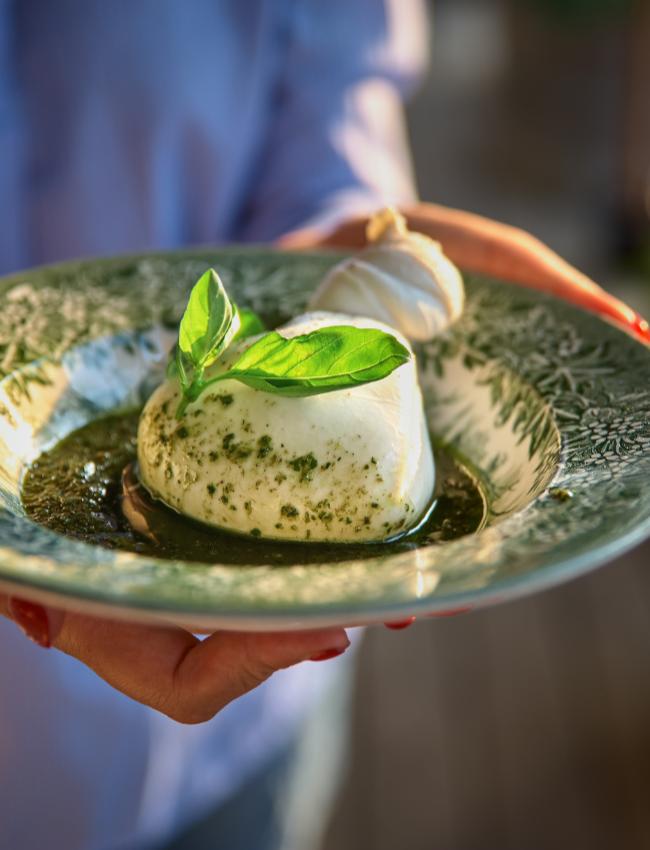 Piatto di burrata con pesto e foglie di basilico su un piatto decorato.