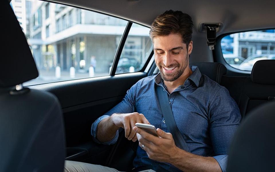 Uomo sorridente in auto, usa il cellulare mentre è seduto sul sedile posteriore.